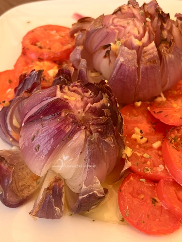 Plato con cebolla asada en forma de flor y rodajas de tomate, regado con vinagreta, lista para servir.