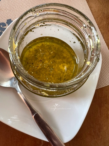 Bote de cristal con ingredientes de vinagreta casera (aceite, lima, mostaza) agitándose para emulsionar.